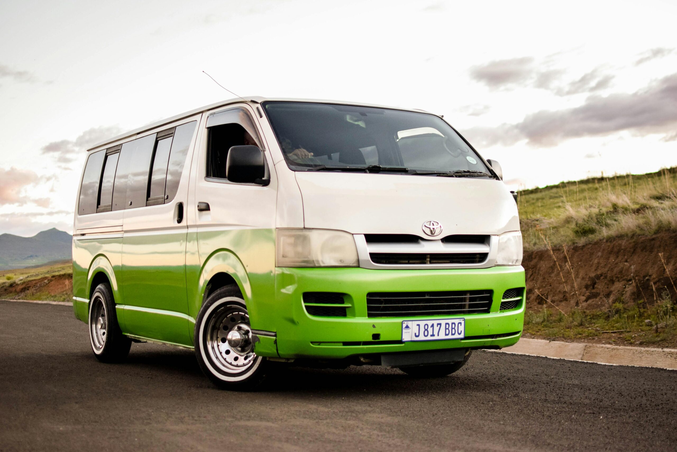 Home A colorful Toyota HiAce van on a scenic road, ideal for travel and transportation themes.
